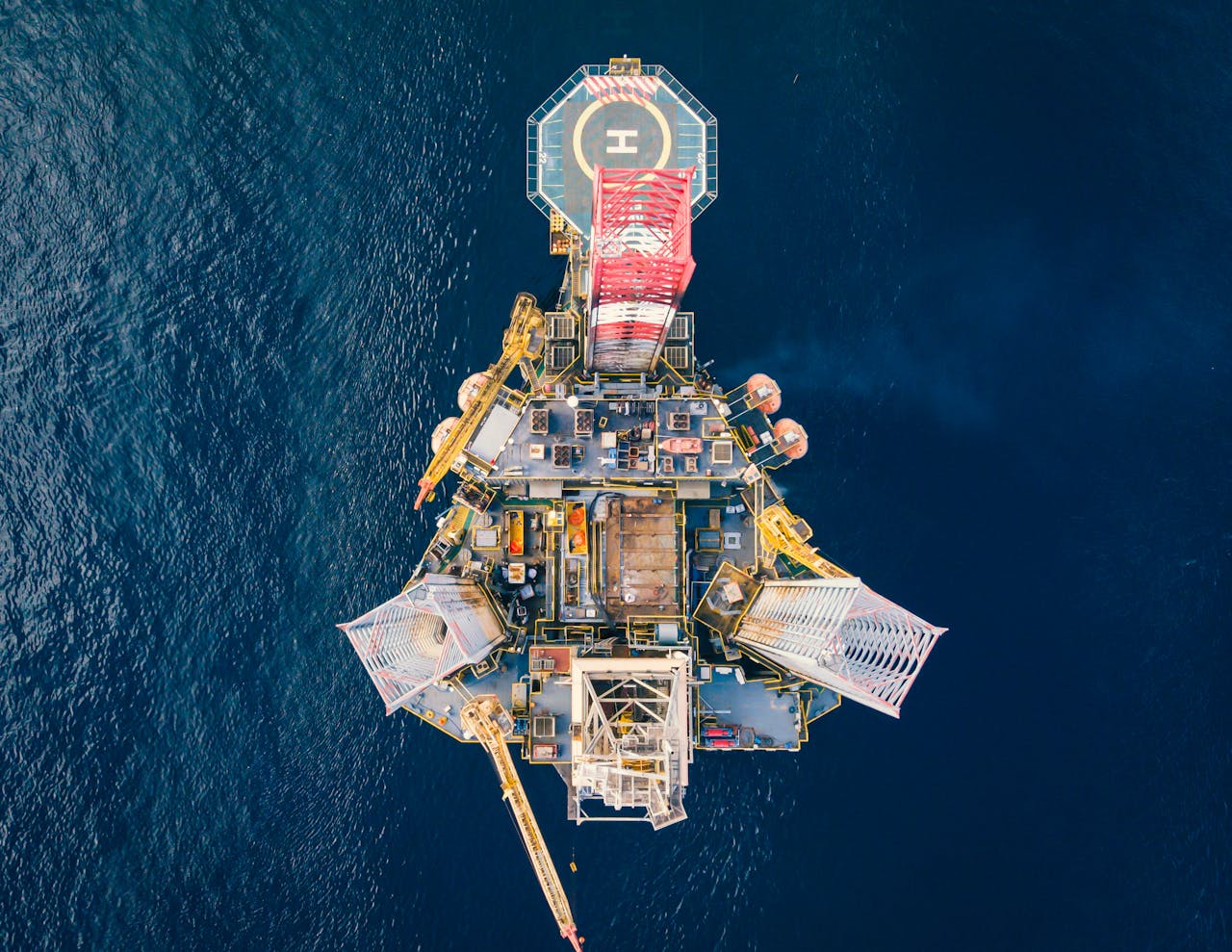 gallery-6 High-angle view of an offshore oil platform with helipad surrounded by deep blue ocean.